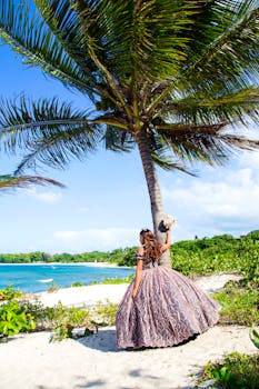 A young girl in a gown celebrates her quinceañera by a palm tree on a beautiful Puerto Plata beach.
