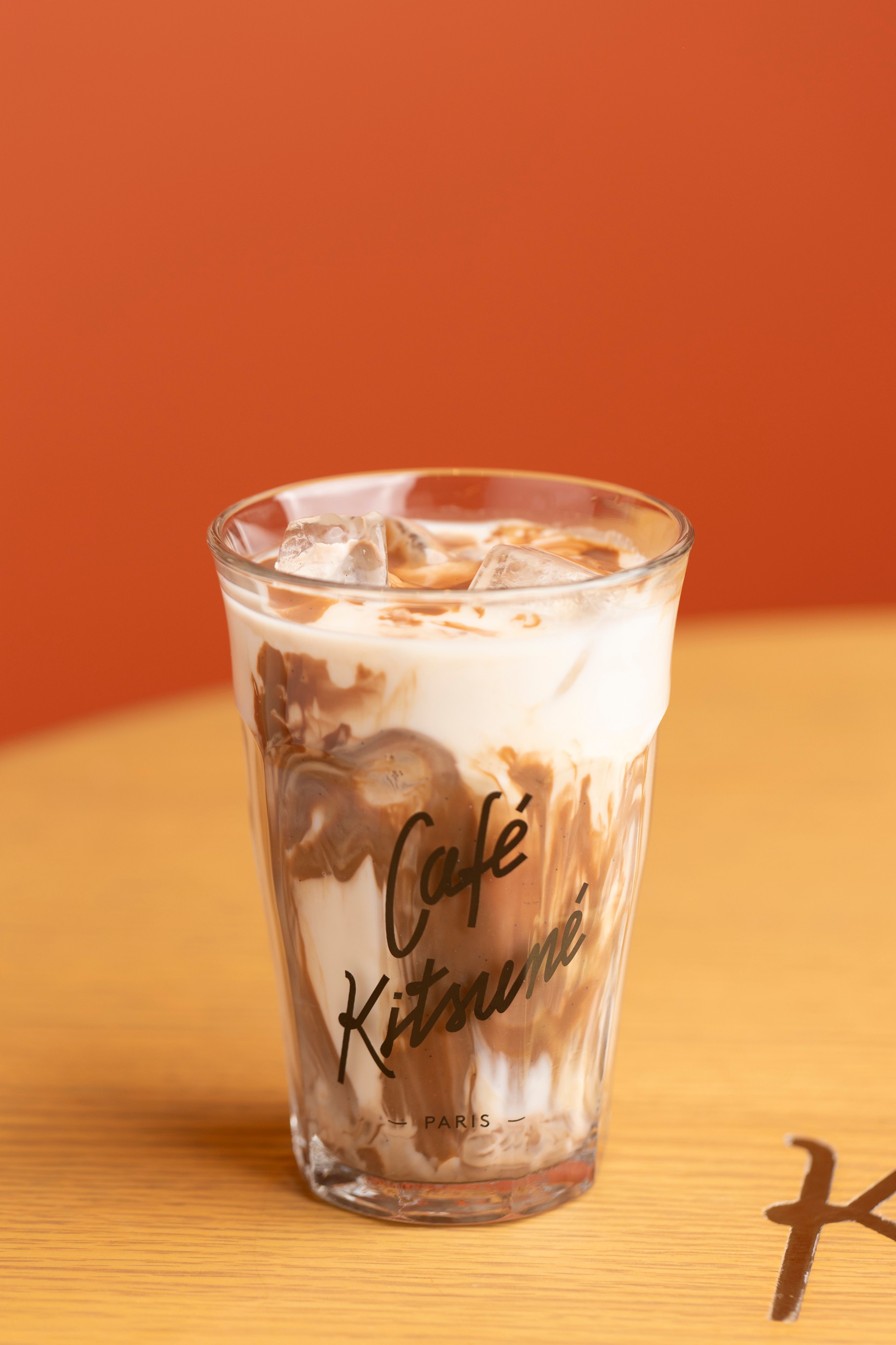 De franc Cafè amb llet fred i gelat al Café Kitsuné sobre una taula de fusta, amb un fons taronja vibrant. Foto d'estoc