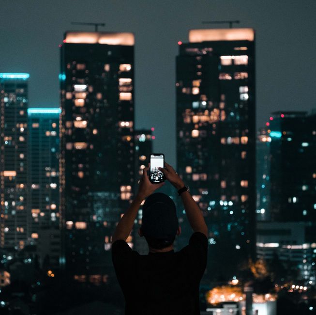 A person photographing Jakarta's illuminated skyscrapers during a vibrant city night. A person photographing Jakarta's illuminated skyscrapers during a vibrant city night.