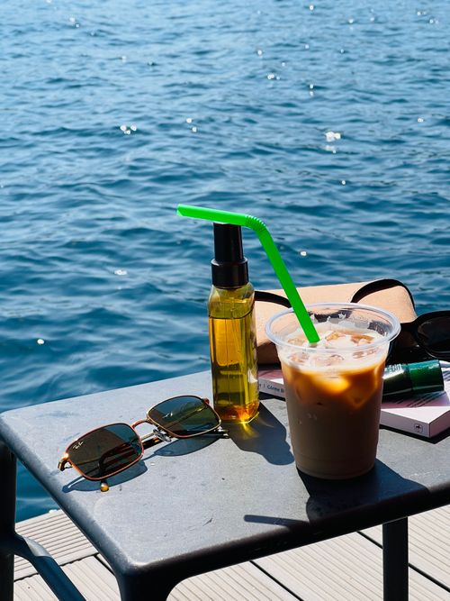 Free Iced coffee and sunglasses by the waterfront on a sunny day. Stock Photo