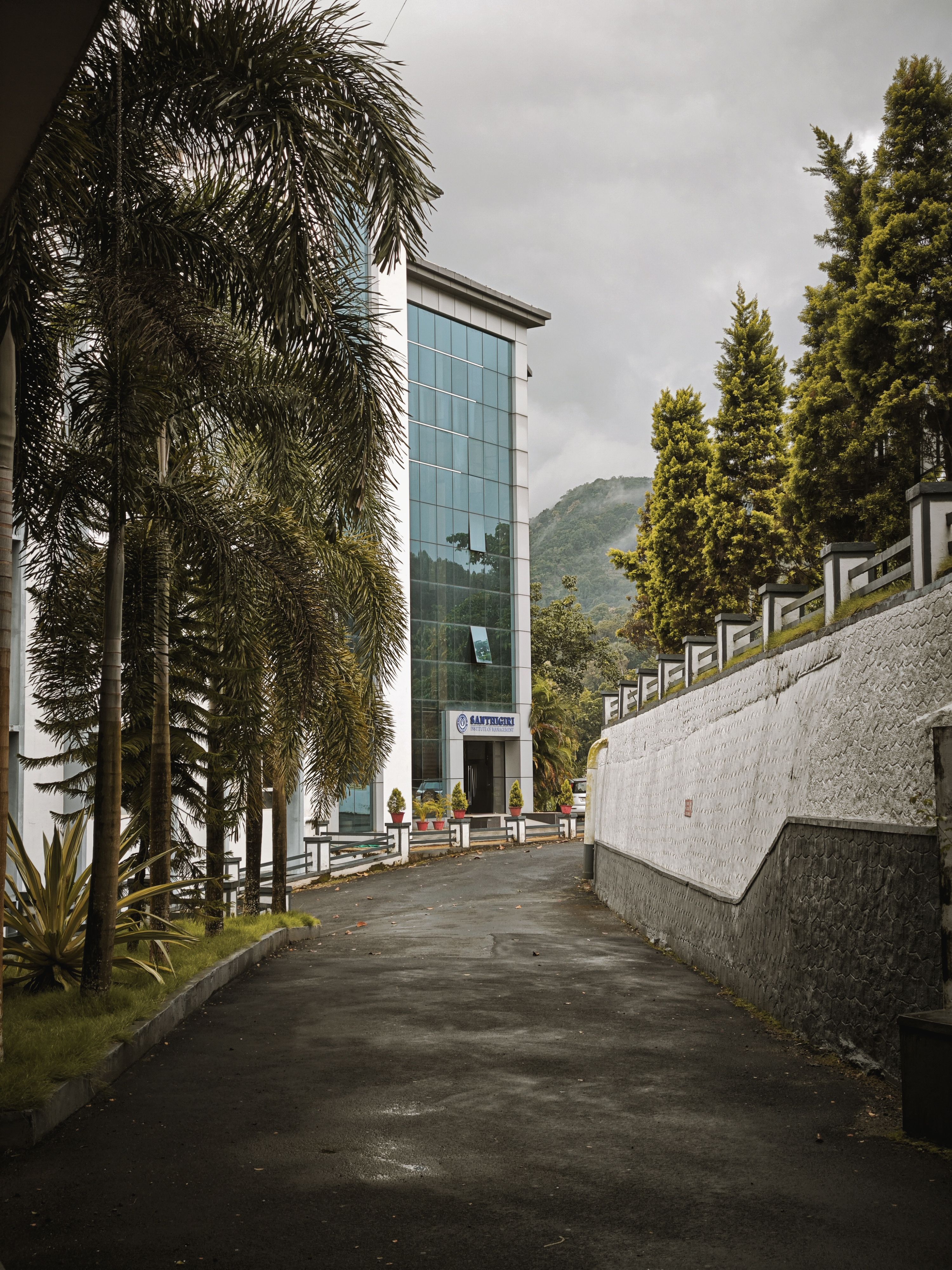 Contemporary building in lush setting, KL India, surrounded by palm trees with mountain backdrop.