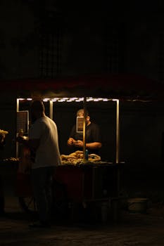 A nighttime street vendor serving food with warm lighting in a dark setting.