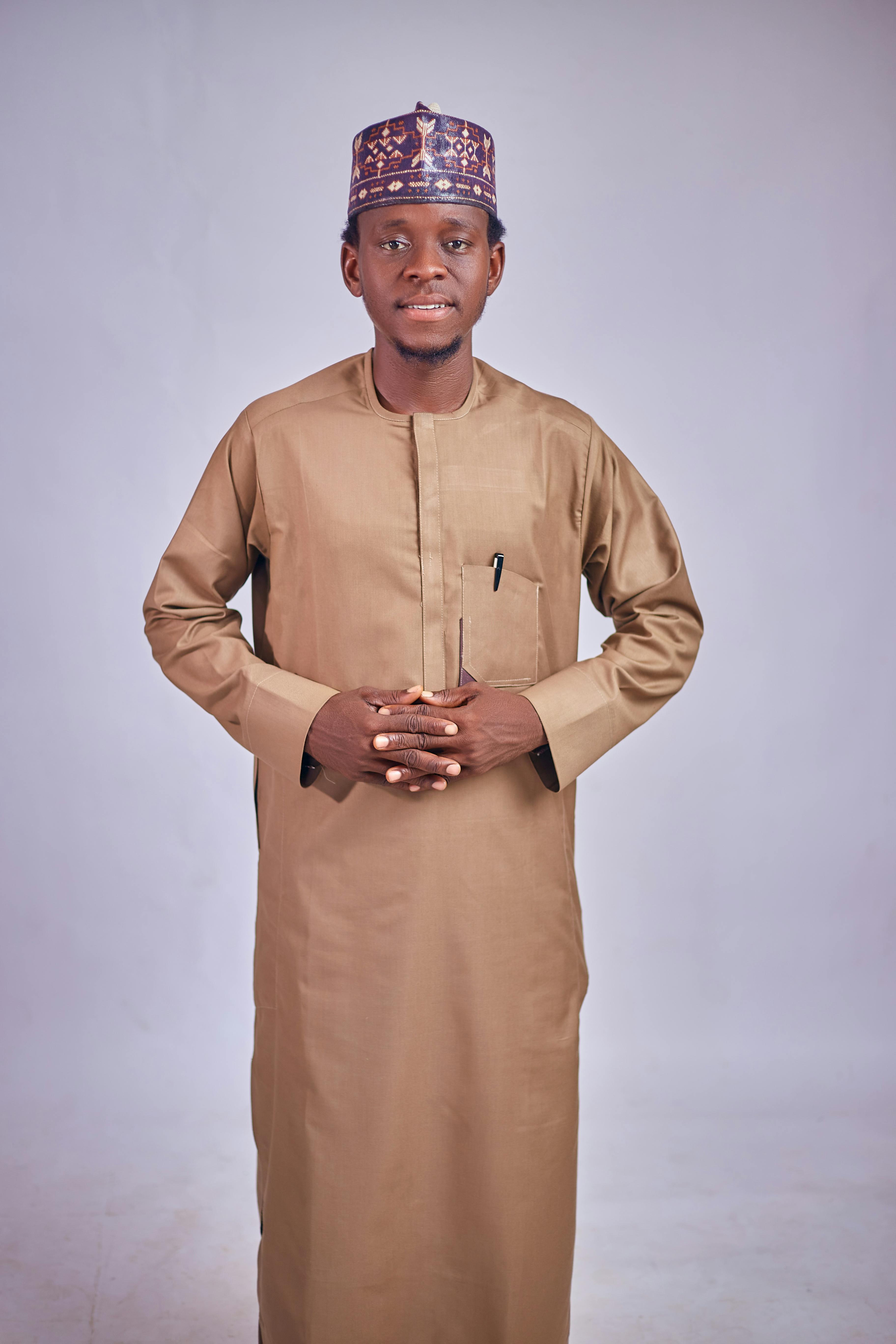 Confident man in traditional African clothing poses against a neutral background.