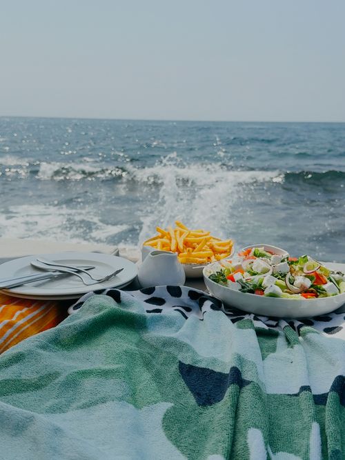Free A scenic seaside picnic setup with fresh salad and crispy fries on a colorful blanket. Stock Photo