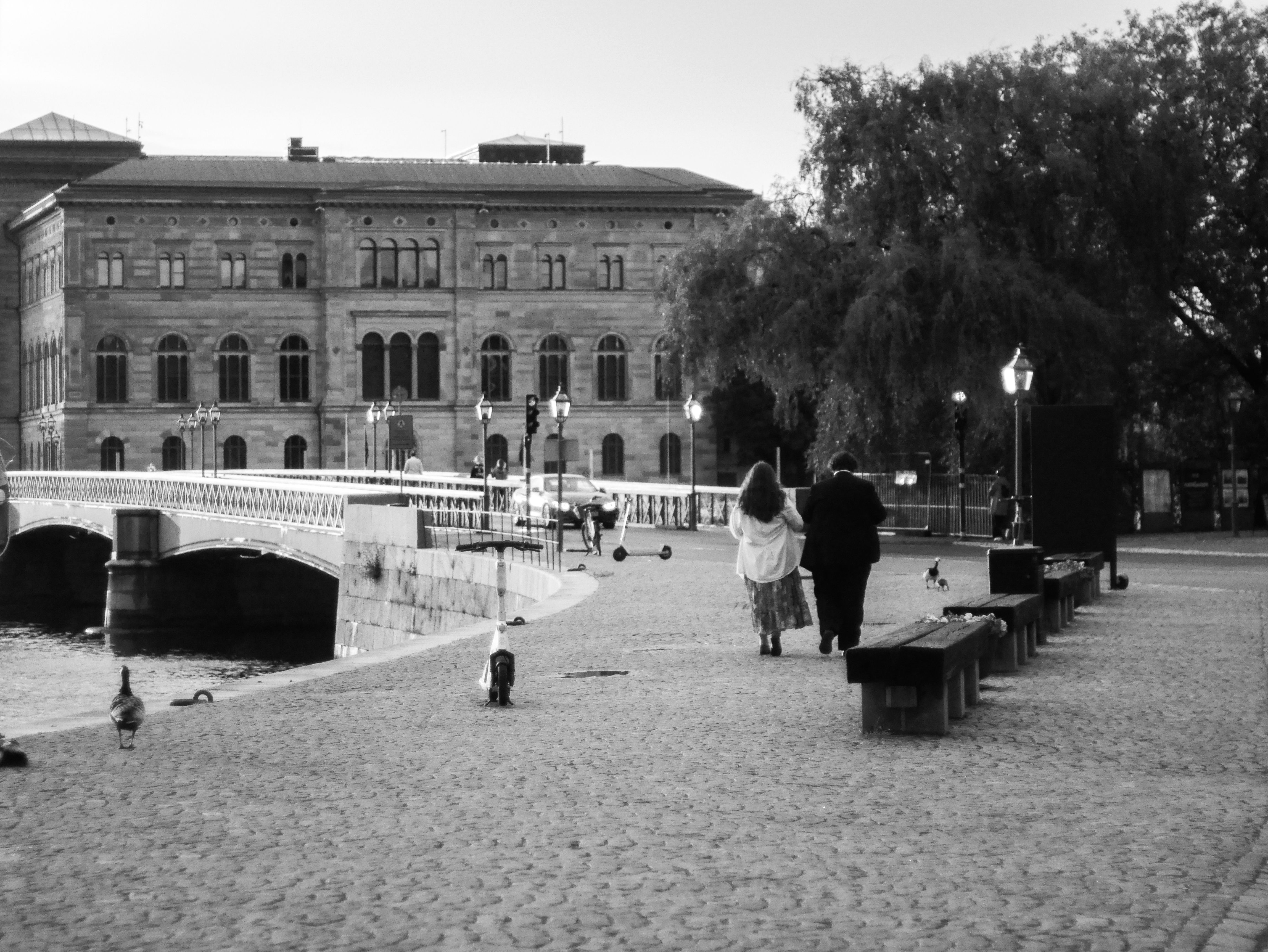 A couple walks along a cobblestone path beside a bridge in Stockholm, Sweden, during dusk. A couple walks along a cobblestone path beside a bridge in Stockholm, Sweden, during dusk.