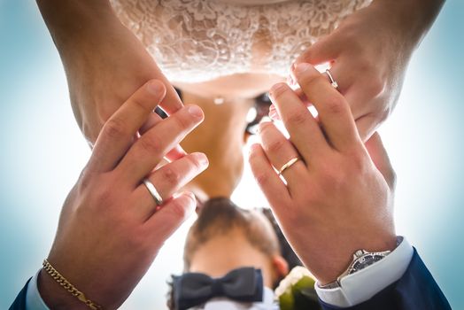 Close-up of a couple's wedding rings and kiss, captured from below with a sky backdrop.