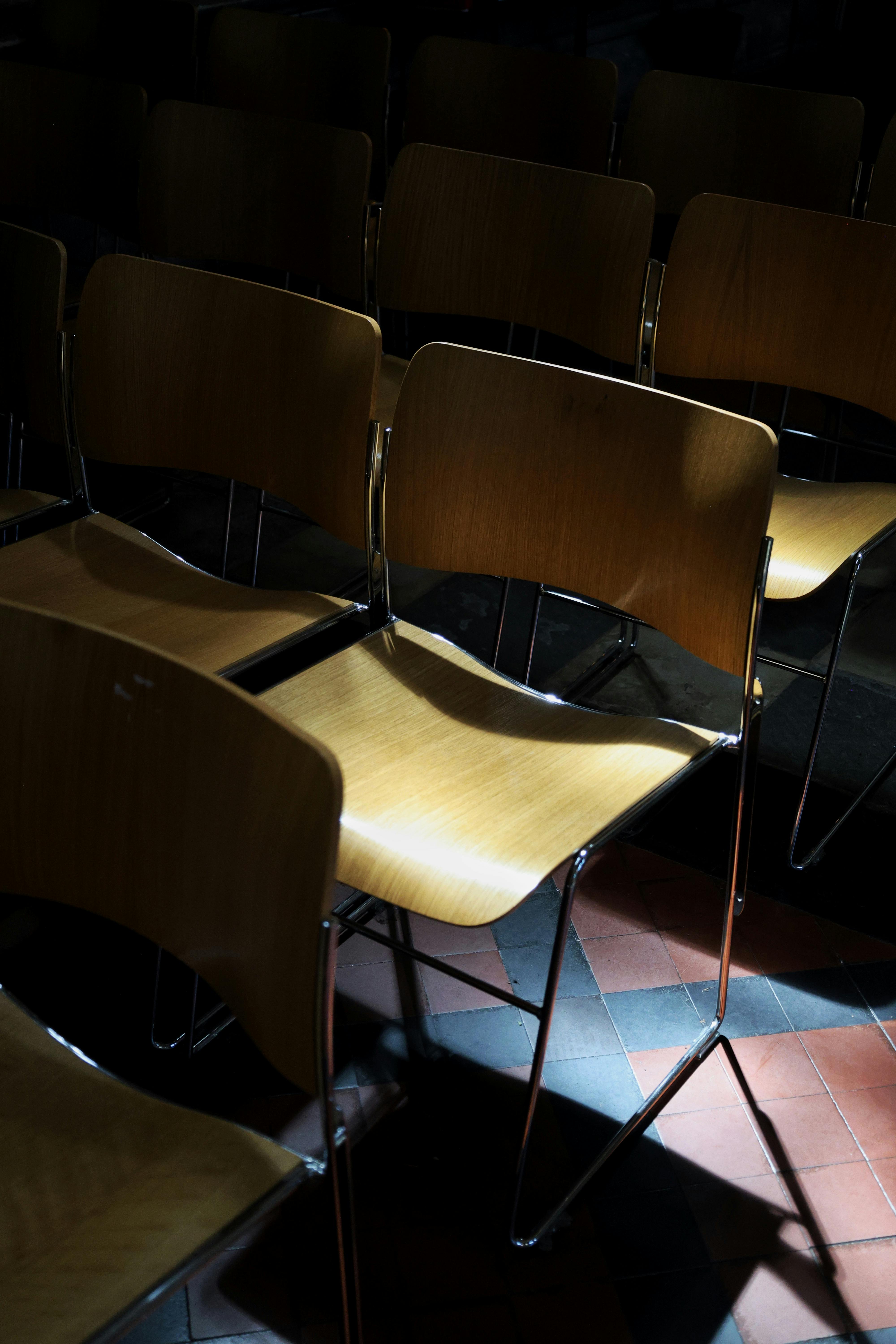 Free Row of wooden chairs in a dimly lit indoor space with tiled floor patterns. Stock Photo