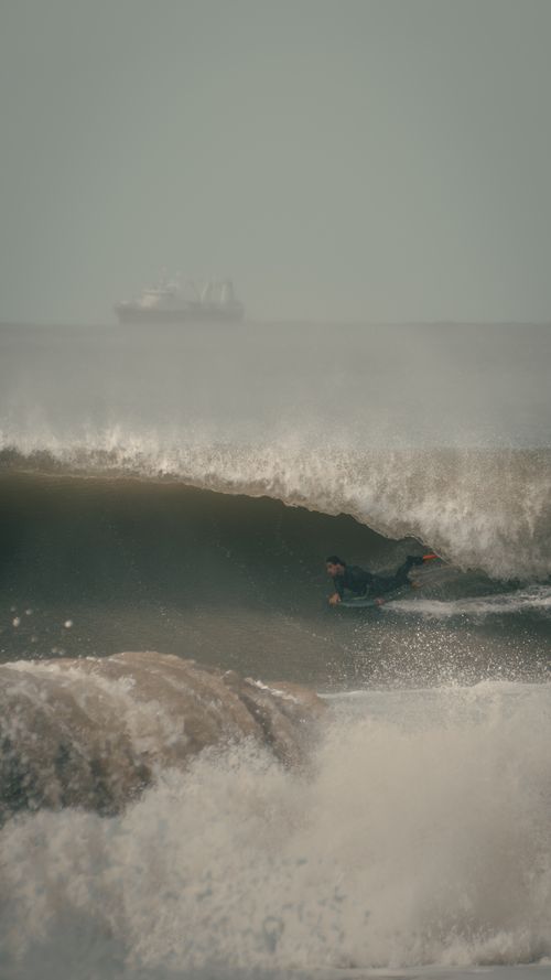 Free Dynamic shot of a surfer catching a wave with a ship on the horizon in Mar del Plata, Argentina. Stock Photo
