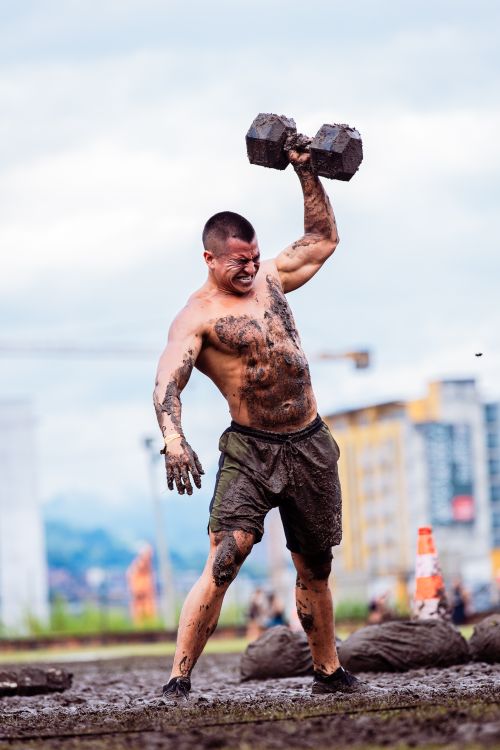 Free Determined athlete lifting weights in a muddy outdoor environment during a fitness competition. Stock Photo