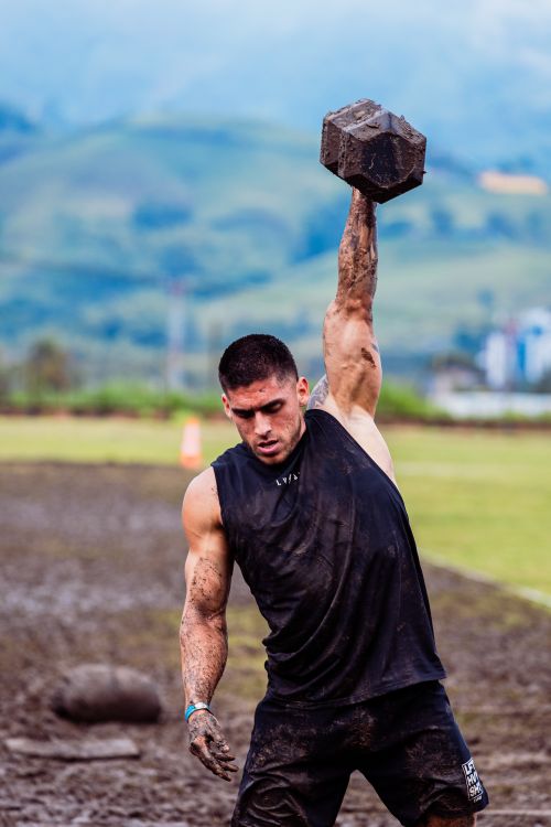 Free Athlete lifting a heavy dumbbell in a muddy field, showcasing strength and determination. Stock Photo