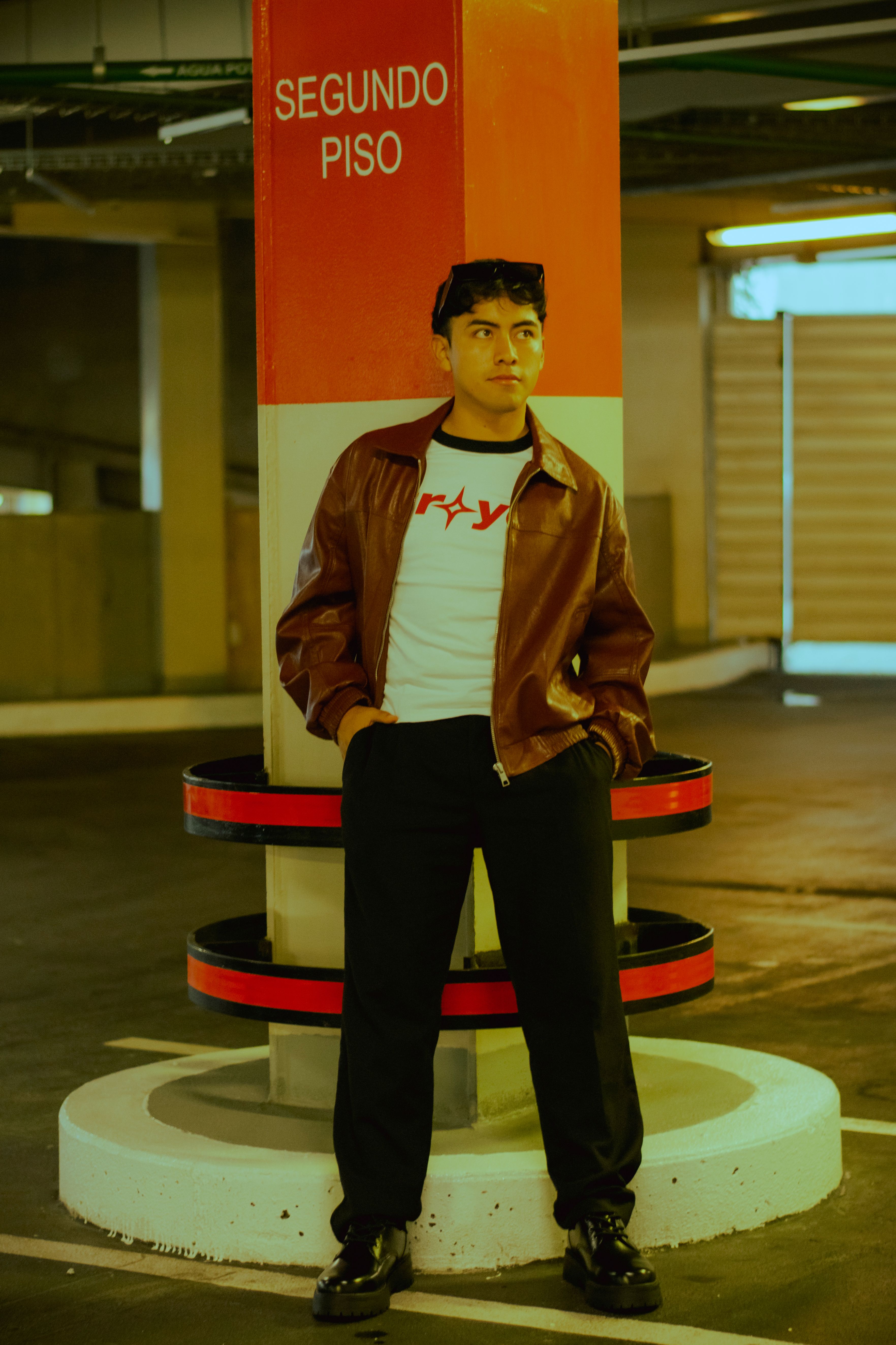 Stylish young man in leather jacket poses in a dimly lit parking garage.