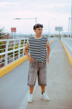 Young man in casual striped outfit on a modern urban overpass during the day.