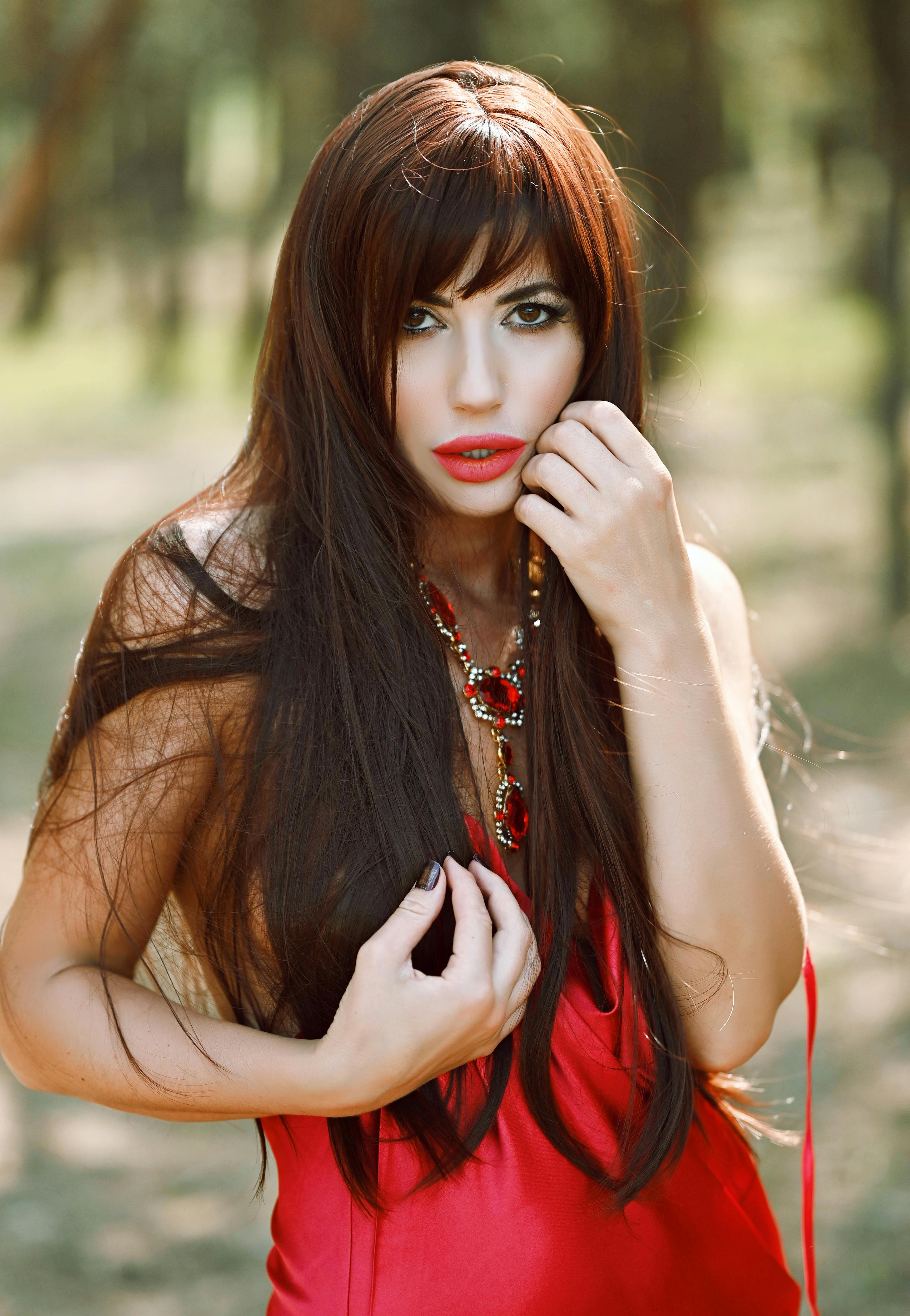 Elegant woman in red dress posing outdoors with long hair and jewelry.