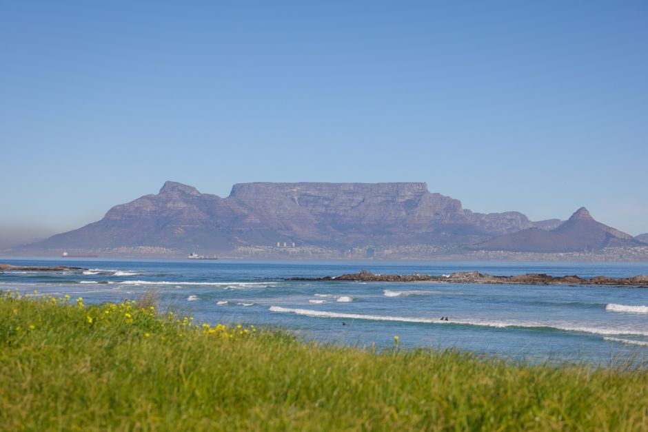 Stunning view of Table Mountain with ocean waves and grassy foreground under clear blue sky.