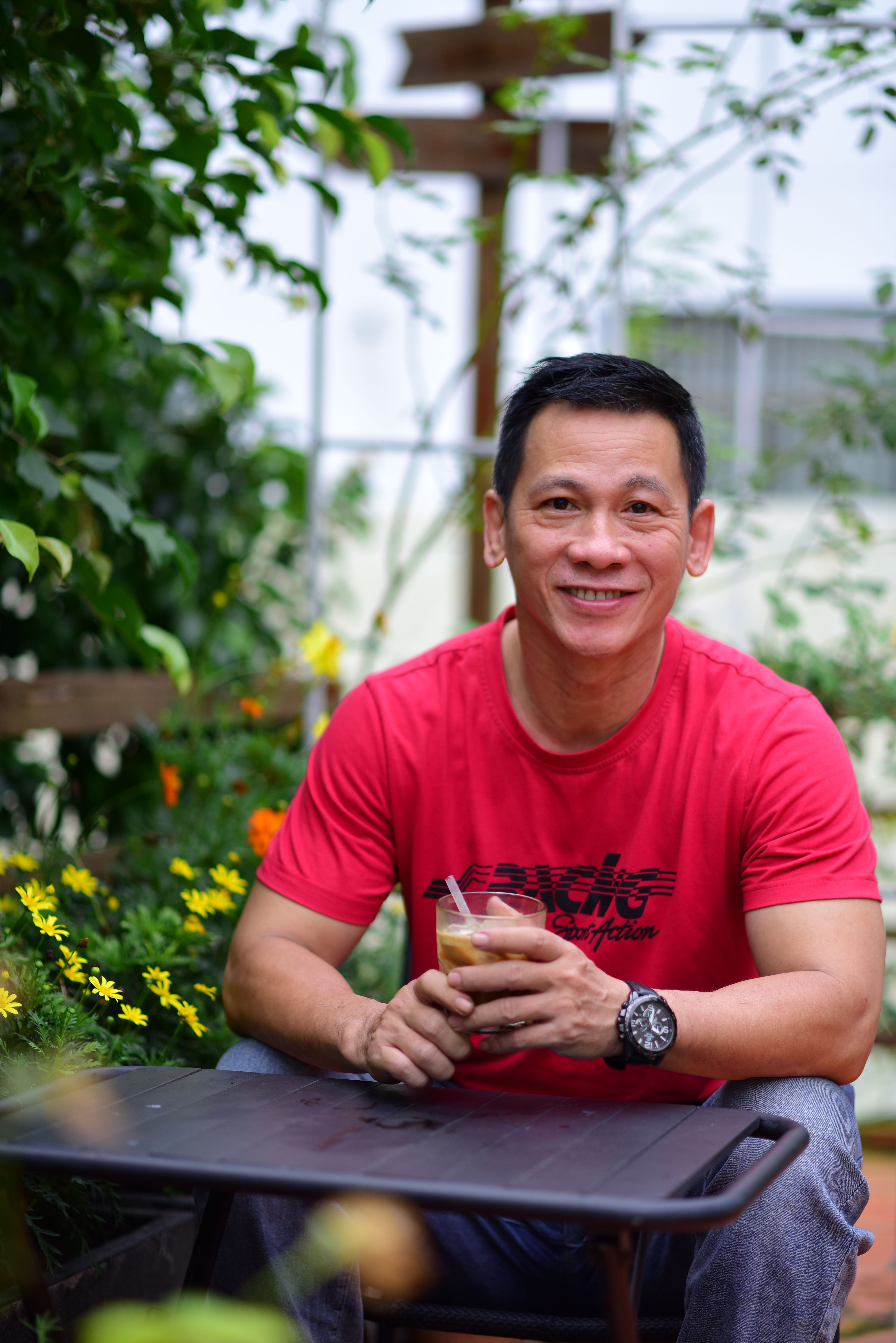 Smiling man in red shirt enjoying a coffee outdoors in a garden, embracing nature and relaxation.