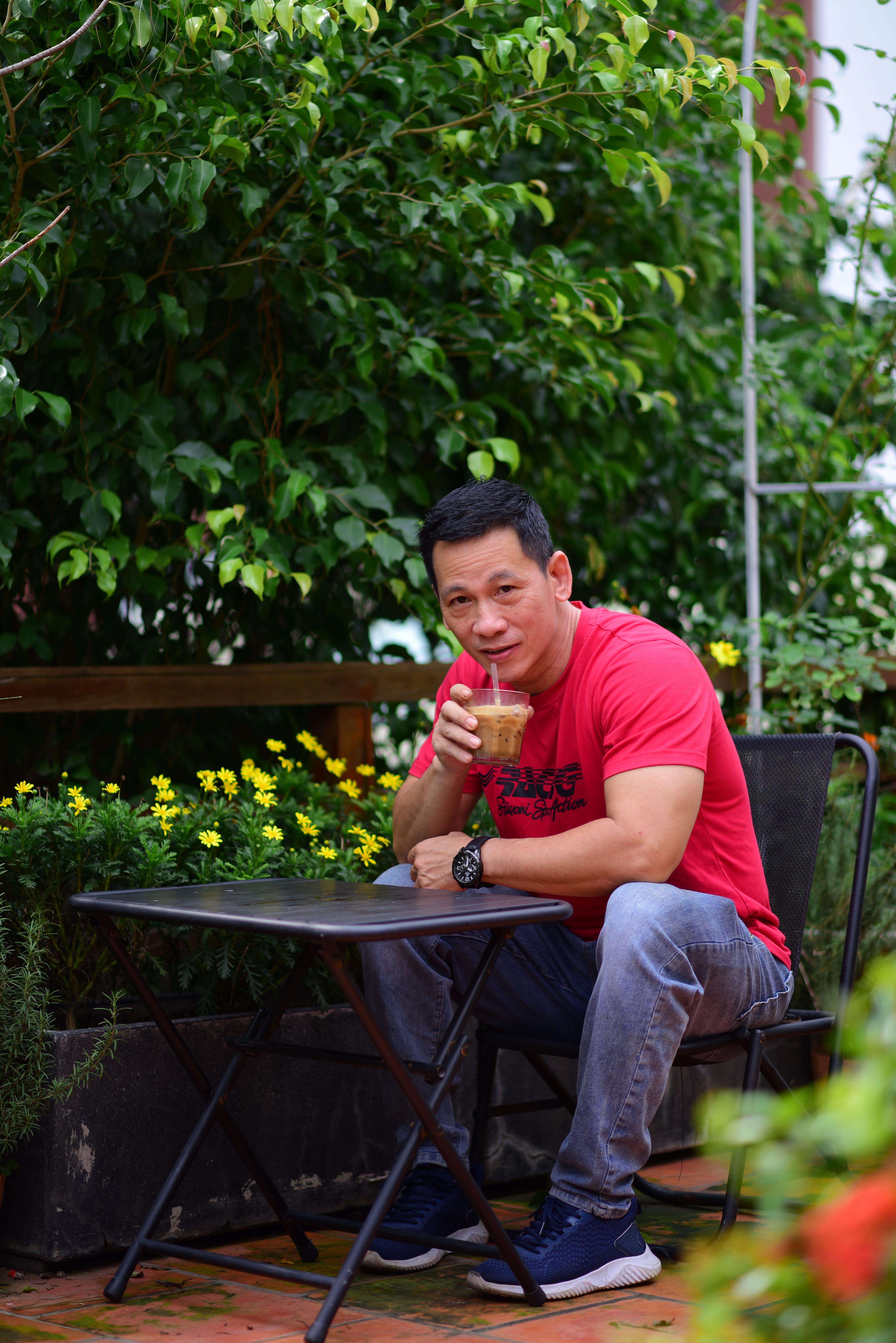 Casual outdoor cafe scene with a man enjoying a coffee surrounded by lush greenery.