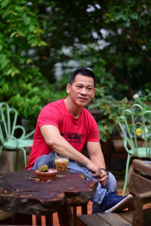 Free Man in red t-shirt enjoying a coffee at a garden cafe with lush greenery. Stock Photo