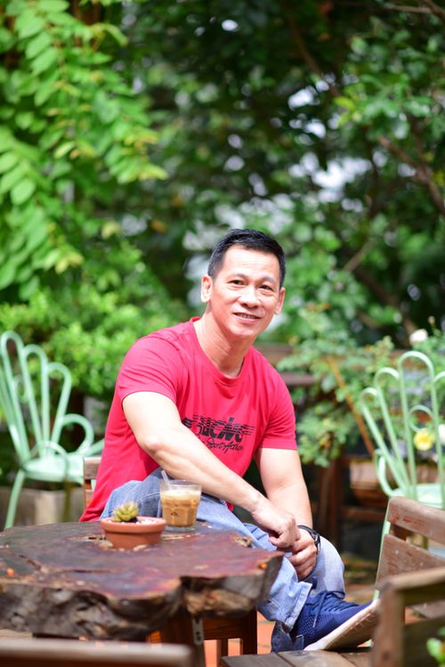 Free A man enjoying his coffee at a garden cafe, surrounded by lush greenery and wooden furniture. Stock Photo