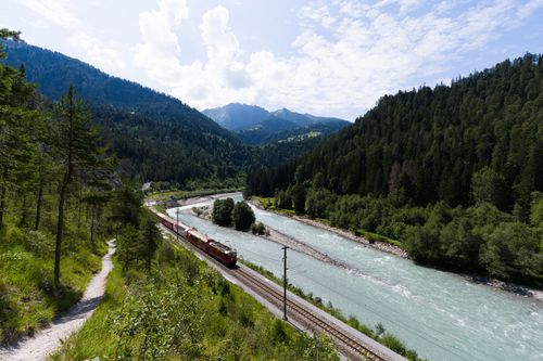 Free Train traversing stunning mountain landscape in Switzerland, showcasing tranquil rivers and lush forests. Stock Photo