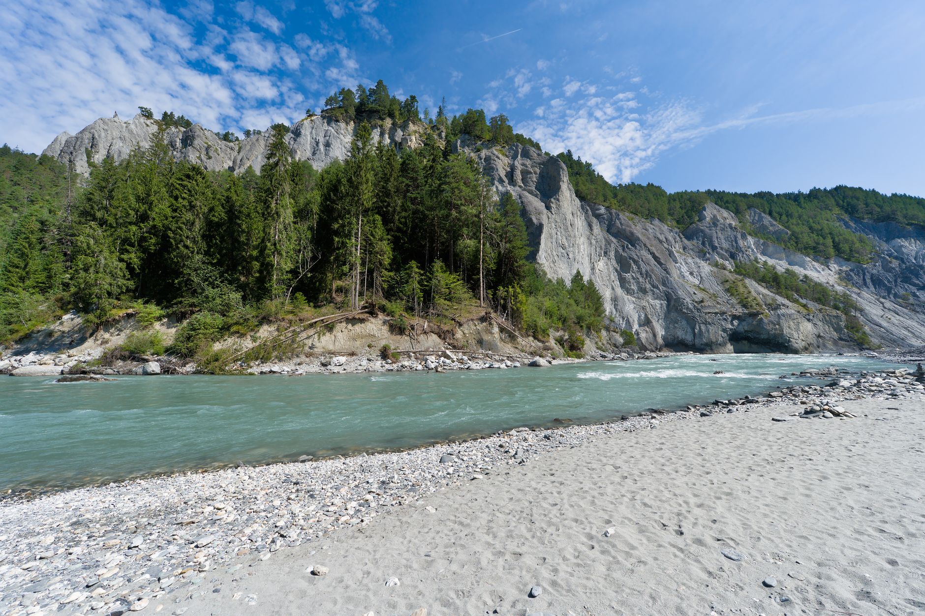 A picturesque view of a river flowing through the Swiss alps under a bright summer sky.