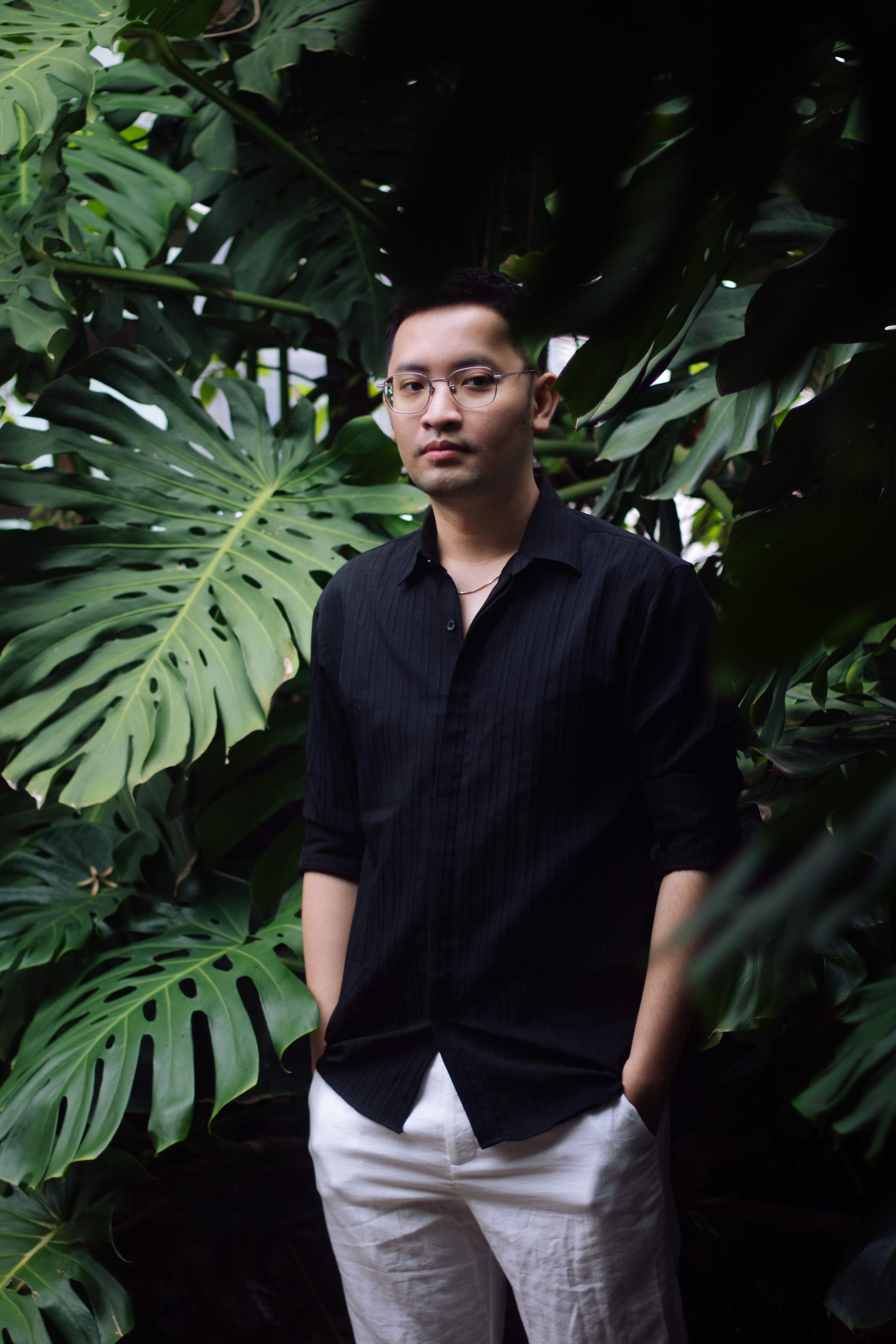 Young man posing in a lush green tropical garden setting, exuding calm and confidence.