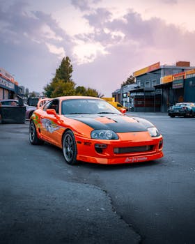 A vivid orange Toyota Supra parked in an open area of Ankara, Türkiye, during a calm day.