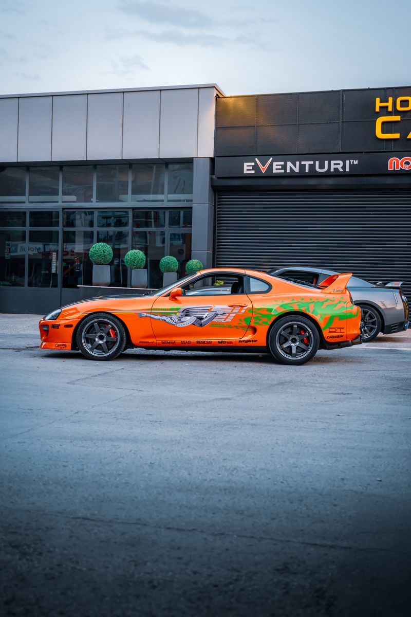 Bright orange Toyota Supra parked in front of a car shop in Ankara, Türkiye, during the day.