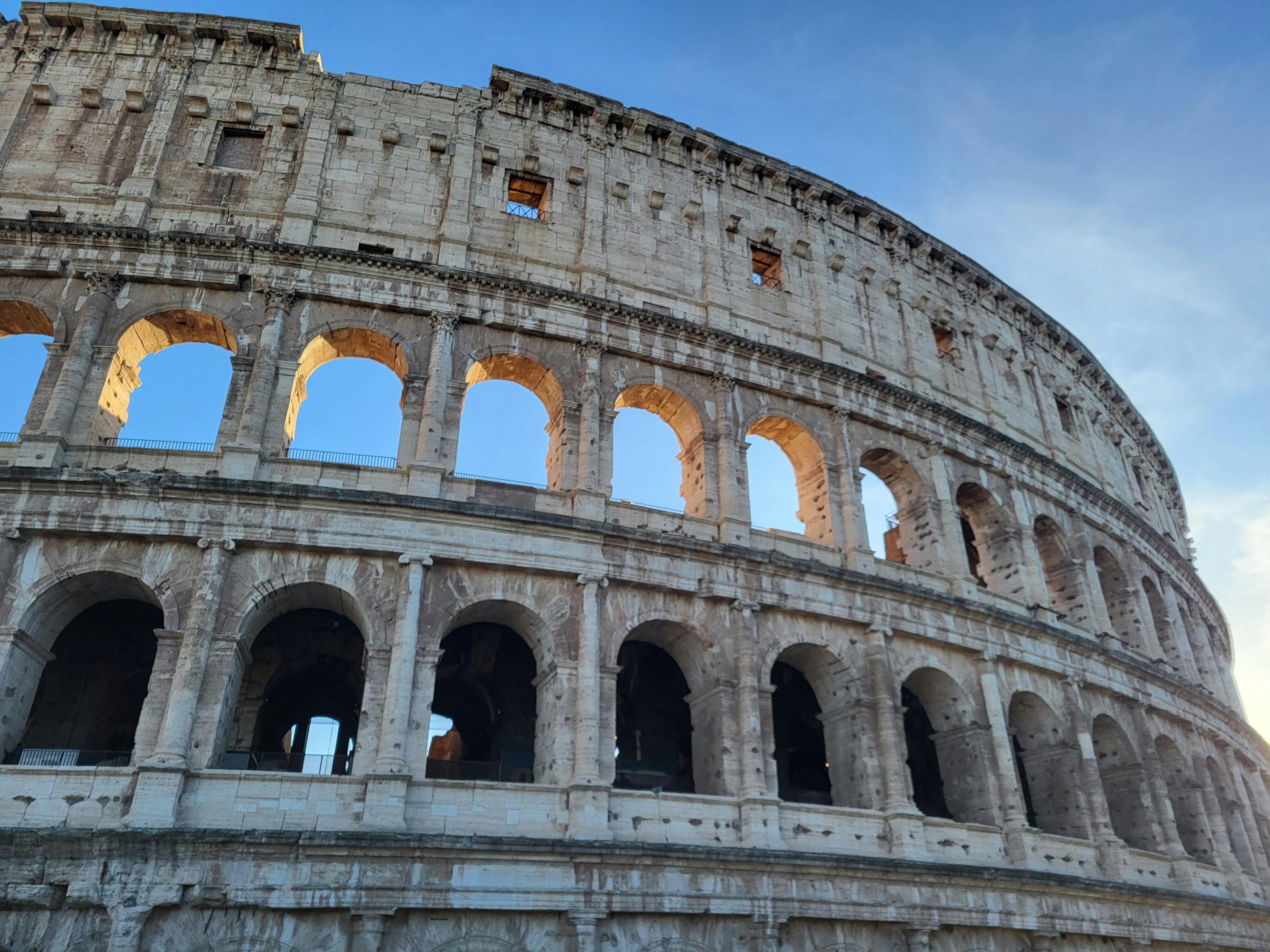 Free View of the iconic Colosseum in Rome with blue sky at sunset. Stock Photo