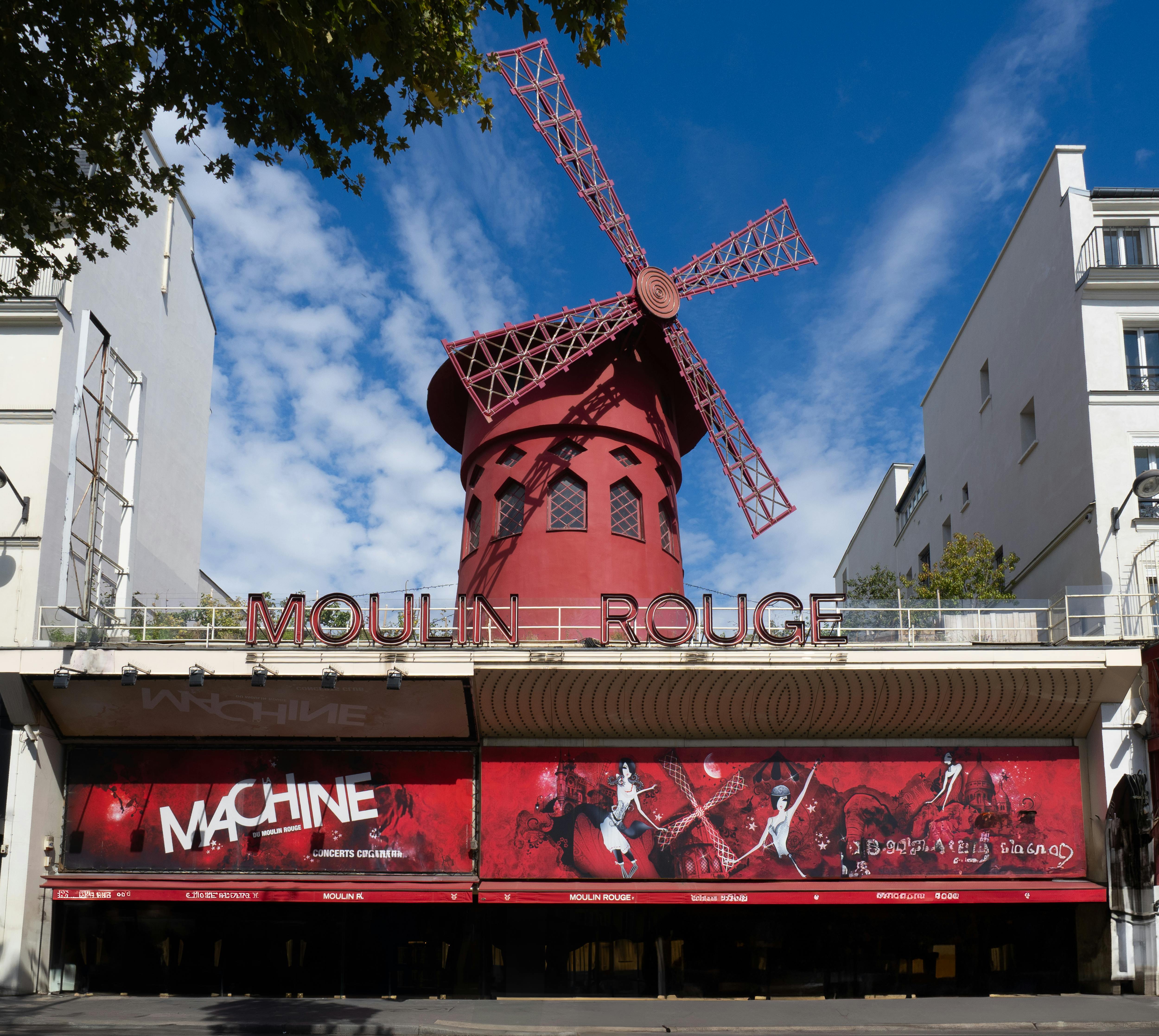 Gratis Kincir angin Moulin Rouge yang ikonik dengan desain merah cerah dengan latar langit biru cerah di Paris, Prancis. Foto Stok