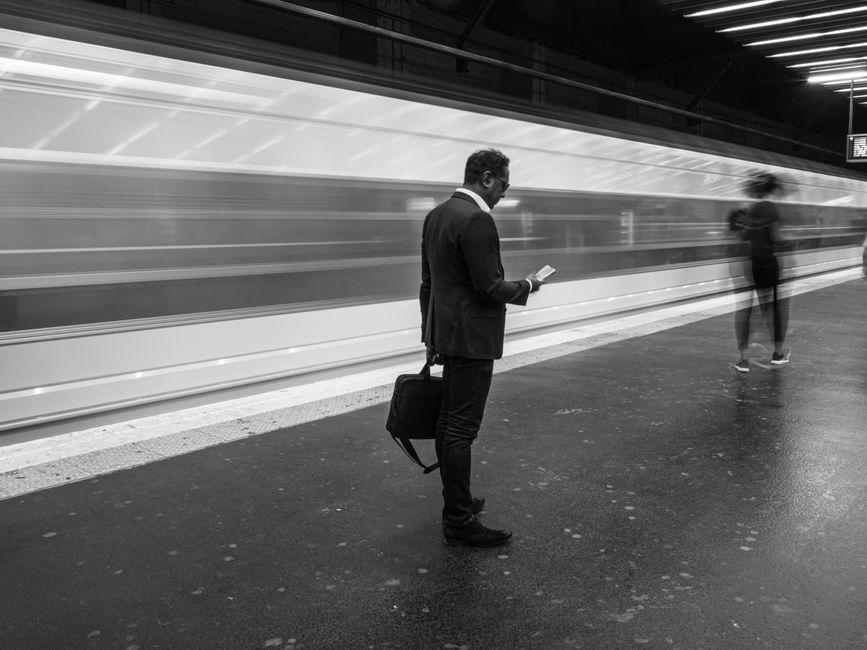 Homem de negócios em estação de metrô movimentada, usando o celular, simbolizando a agilidade e inovação em agências.