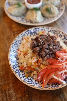 Delicious Uzbek plov with beef, served with dumplings on decorative blue plate.