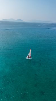 Solo sailboat gliding on the tranquil turquoise sea under clear skies, conveying peace and freedom.