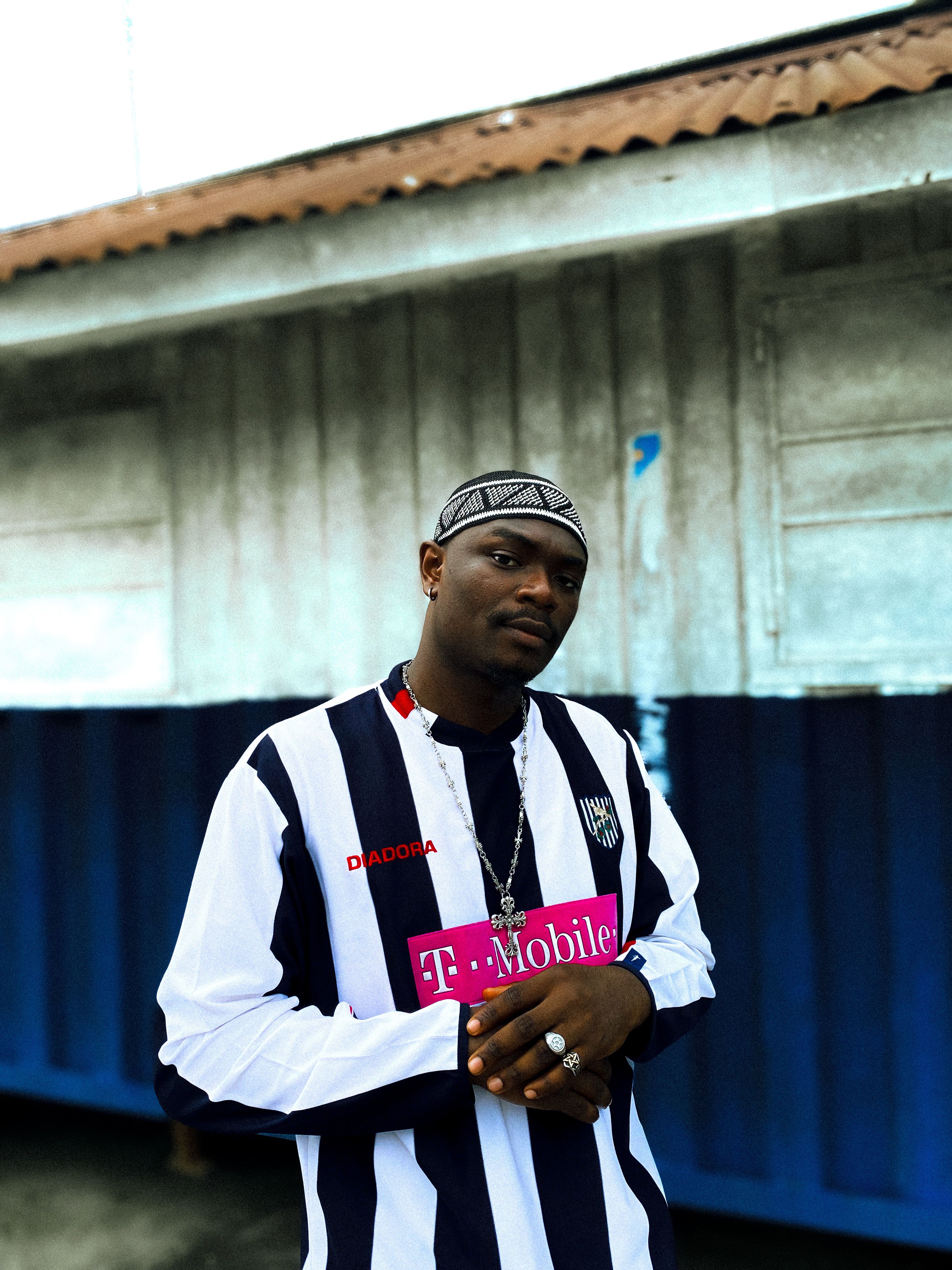 Portrait of a confident young man in a striped jersey, standing outdoors with a casual pose.