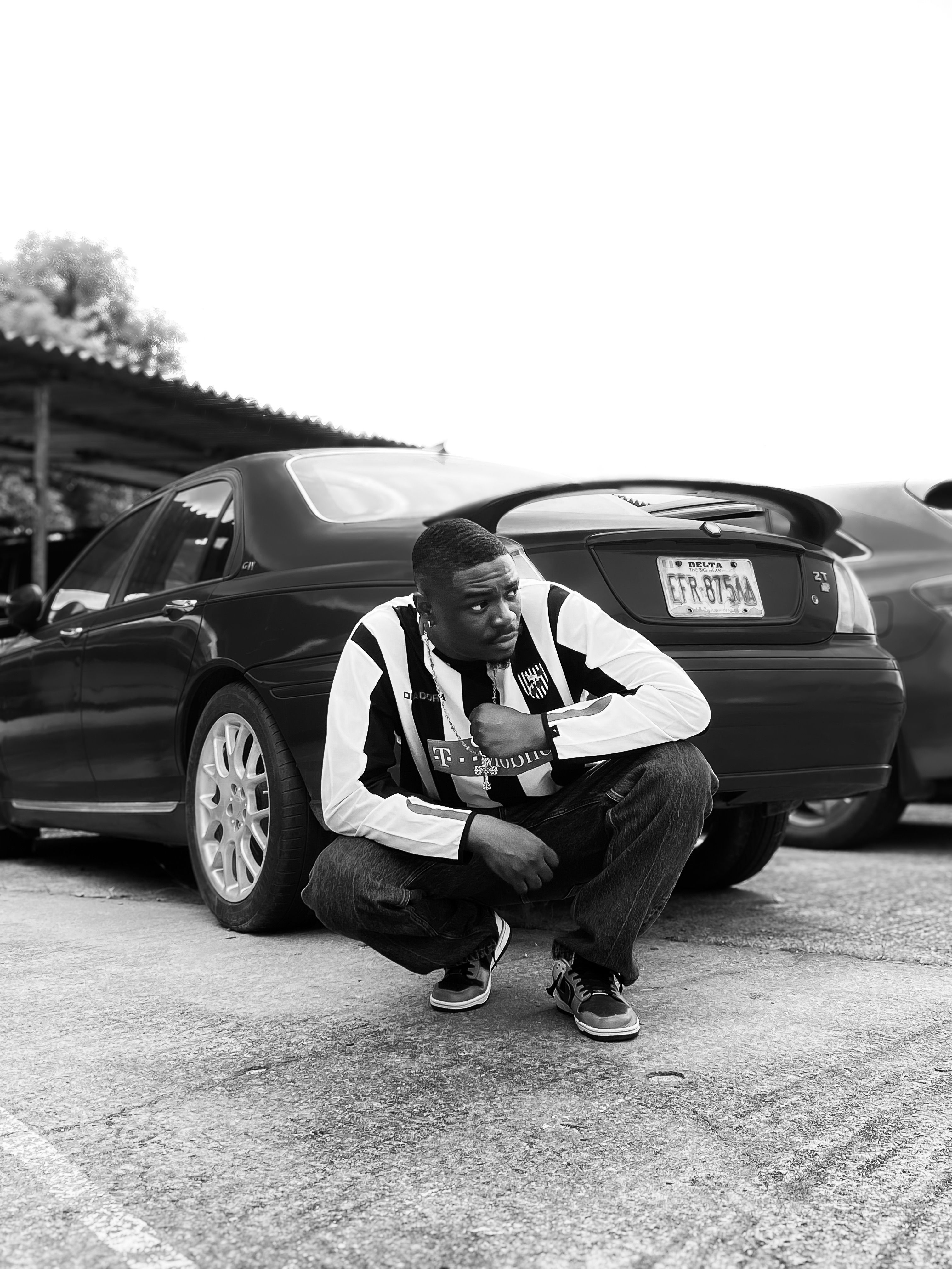 Man crouching beside black car in urban setting · Free Stock Photo