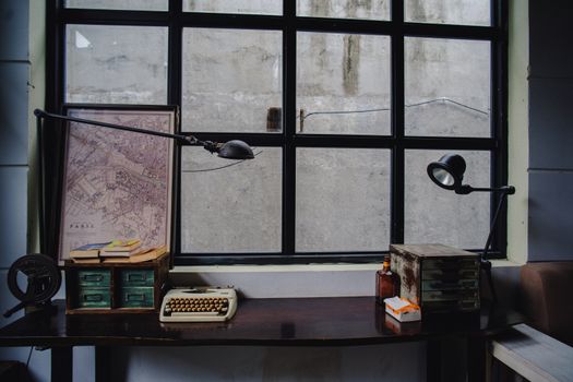 A vintage office desk setup featuring a typewriter, Paris map, and classic decor by a window.