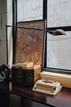 Cozy vintage workspace featuring a typewriter, map, and books by a window.