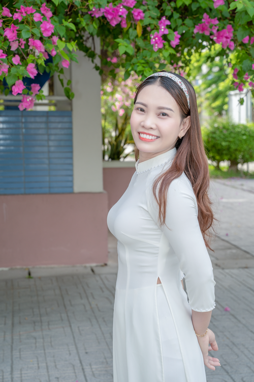 Free Portrait of a smiling woman in a white dress, framed by flowers outdoors. Stock Photo