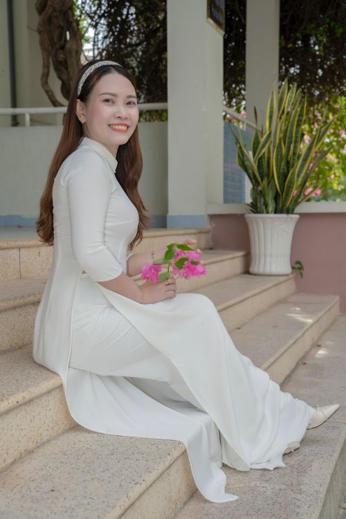 Free Smiling woman in white dress sitting on steps holding flowers. Stock Photo