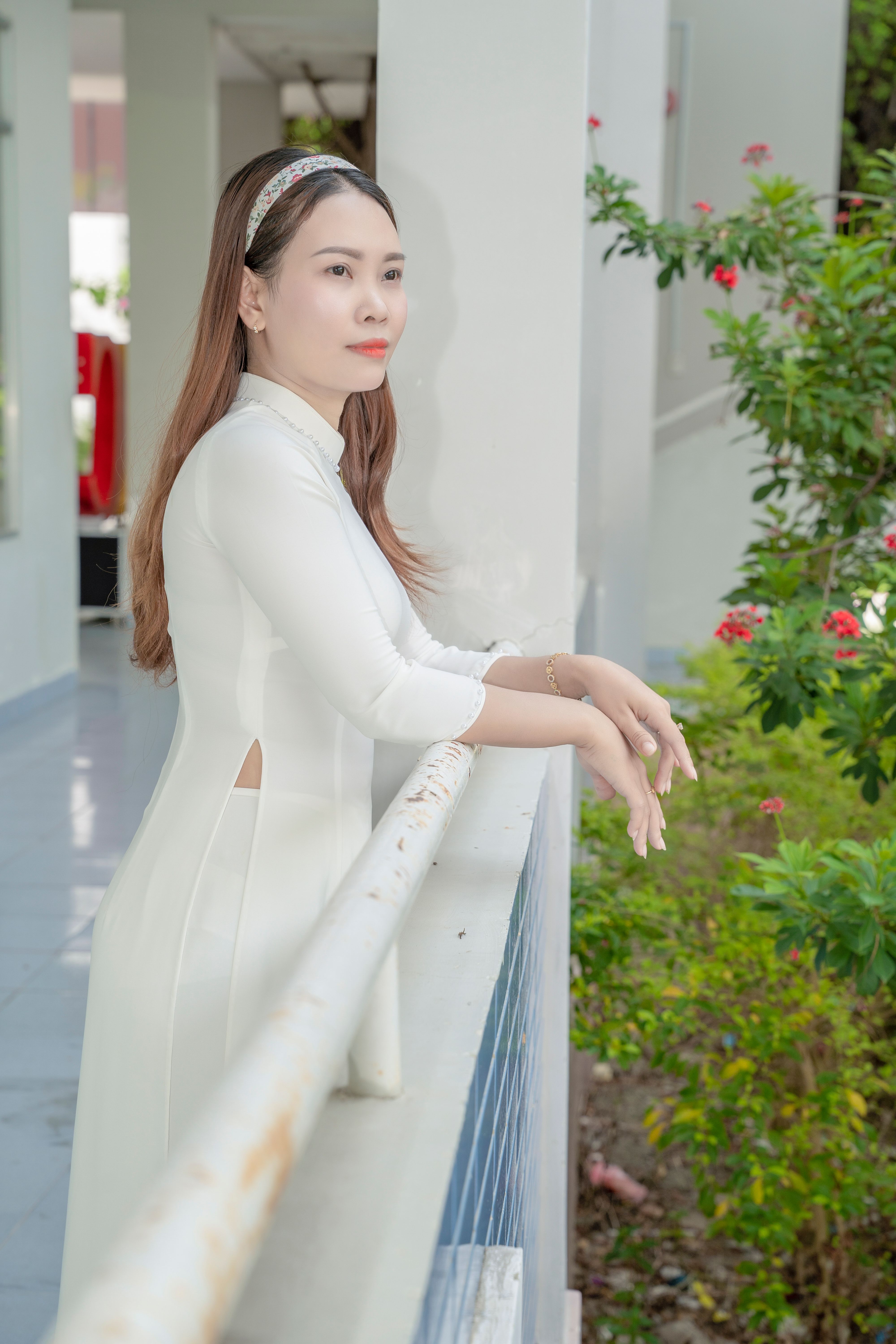 Asian woman in traditional white dress standing on a balcony, gazing thoughtfully.