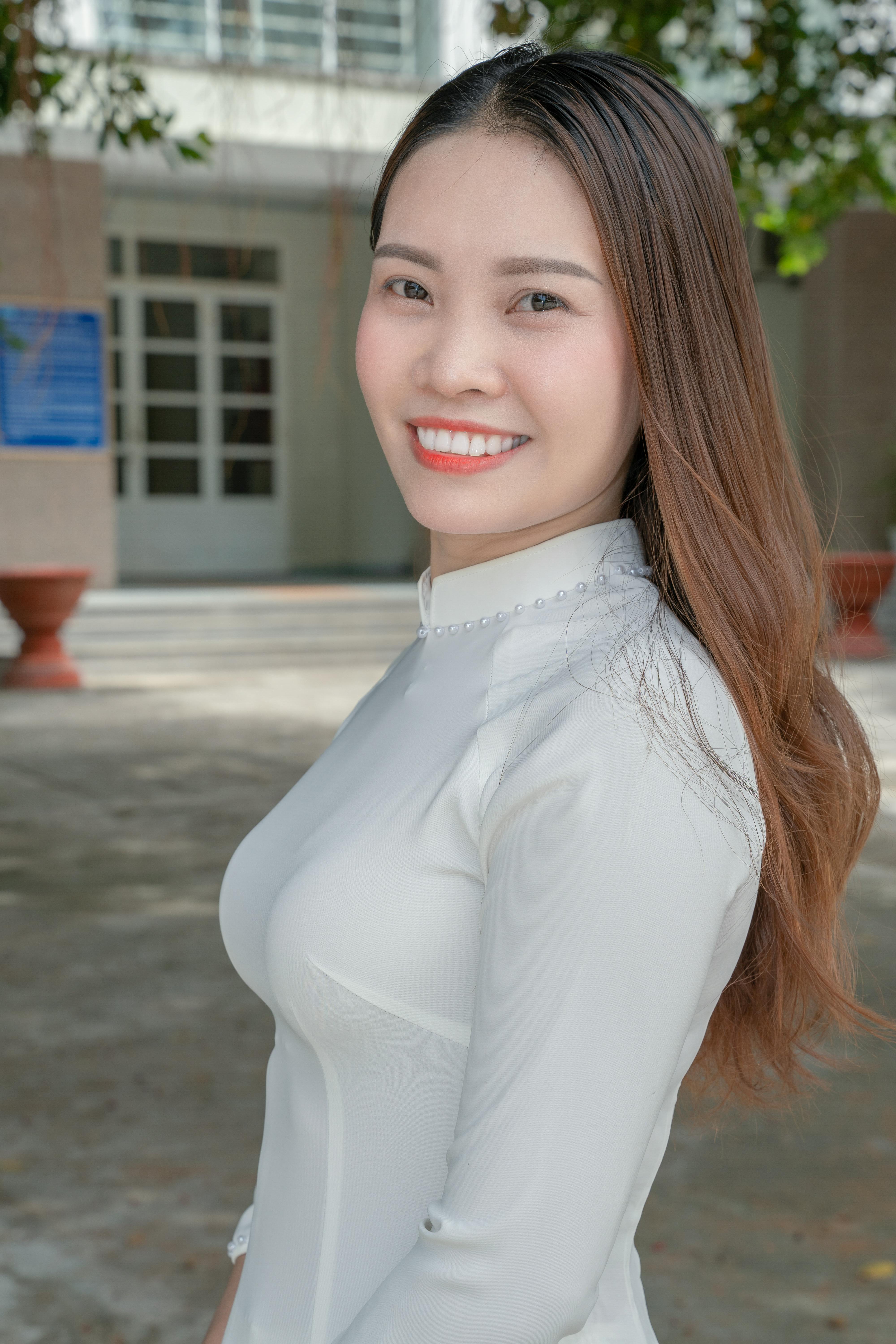 Smiling woman in a white dress outside a building, exuding confidence and elegance.