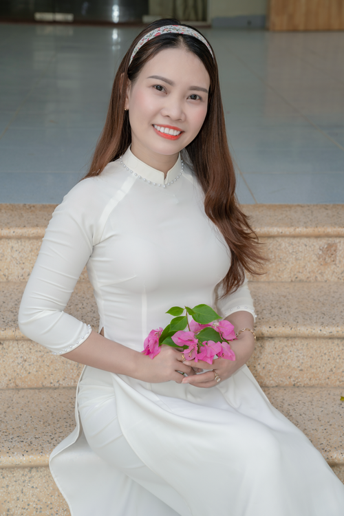 Free Smiling woman in white dress holding pink flowers on stone steps. Stock Photo