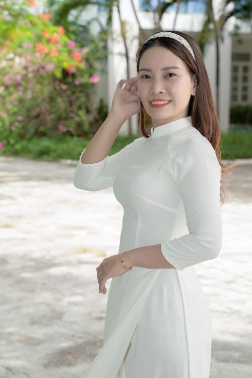 Free Young woman wearing traditional white áo dài dress, standing outdoors. Stock Photo