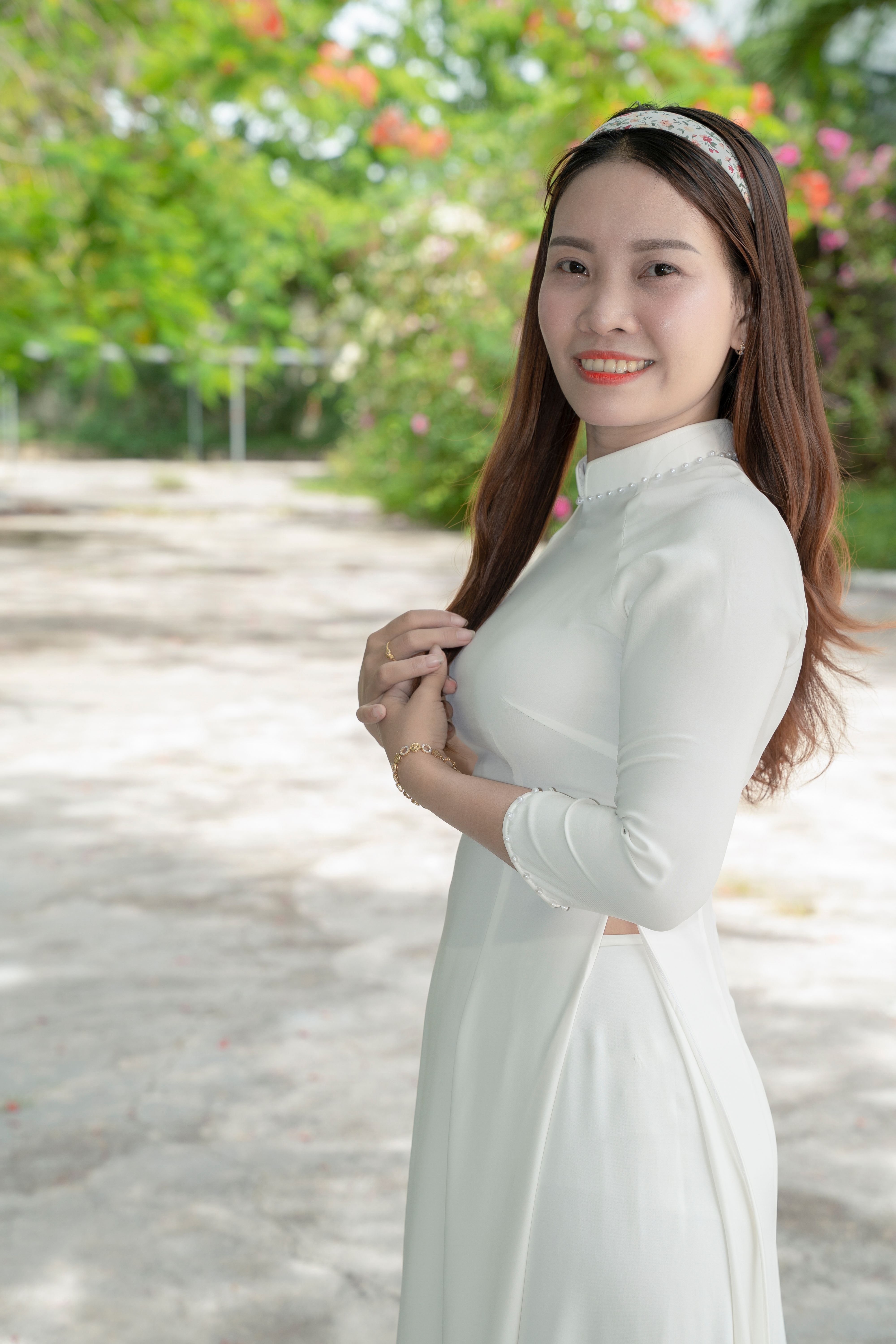 Young woman in white ao dai dress smiling outdoors, bright day