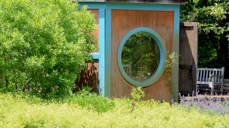 A timber garden hut with a round window among greenery