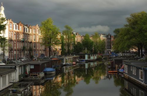 Free Picturesque view of Amsterdam's serene canal lined with houseboats and historic buildings. Stock Photo