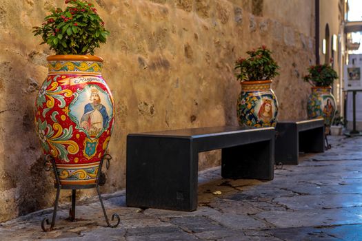 Vibrant ceramic pots adorn a rustic alleyway in Sicily, Italy, emphasizing traditional craftsmanship.