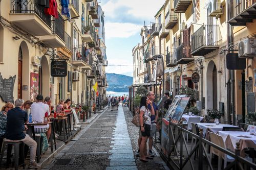 Free Vibrant street scene in Sicily, Italy with bustling cafes and scenic ocean view. Stock Photo