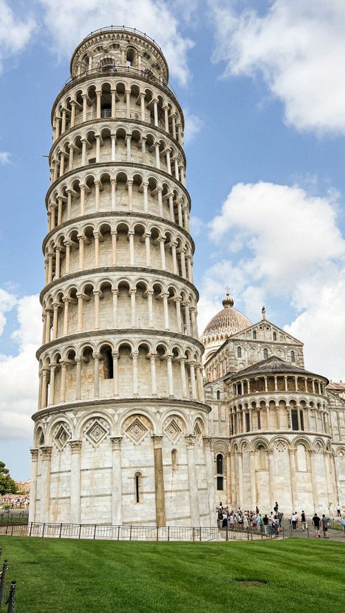 Free Iconic Leaning Tower of Pisa under a bright blue sky with scattered clouds. Stock Photo
