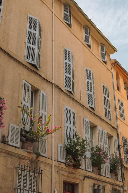 Elegant European building facade with shuttered windows and flower-filled balconies under a clear sky.