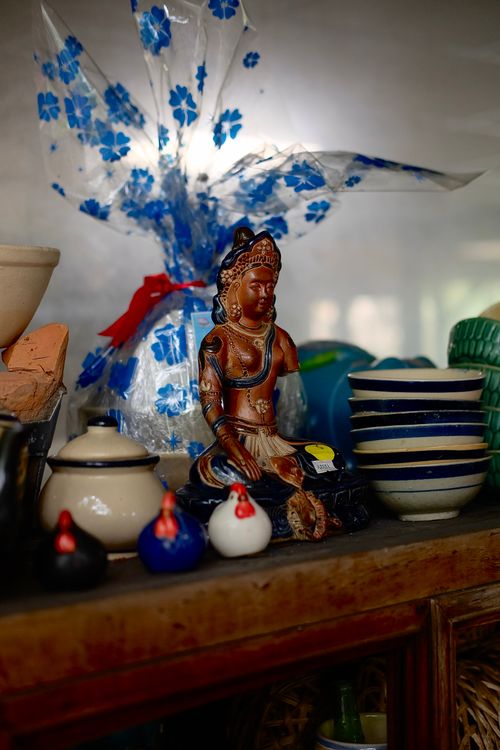 Free Decorative Buddha statue surrounded by ceramic dishes on a wooden shelf, warm atmosphere. Stock Photo